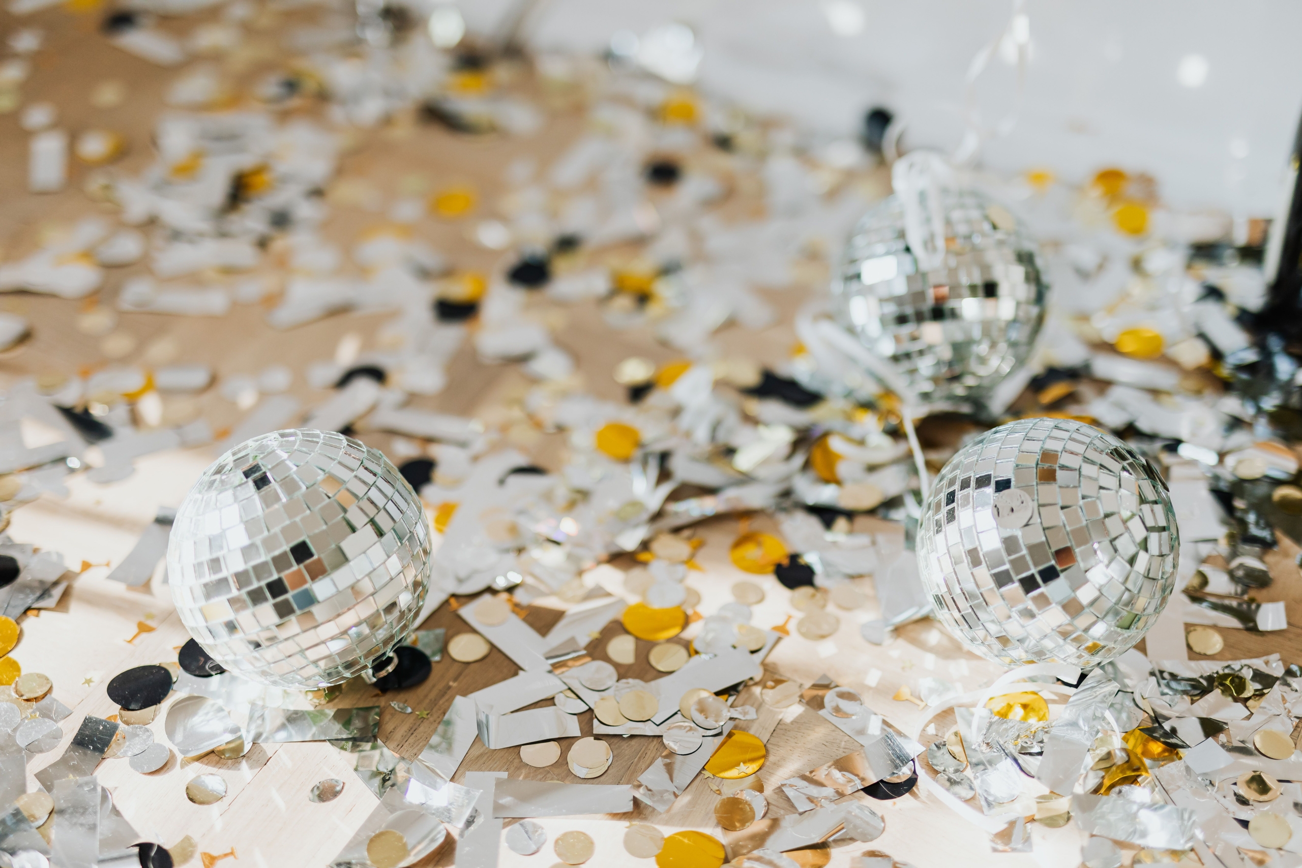 Three disco balls and confetti scattered on the floor in bright light.