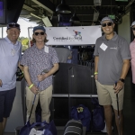 Four men in casual golf attire pose indoors with golf clubs, smiling in front of a Certified Federal Credit Union sign. Golf bags and equipment are visible around them.