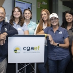A group of eight smiling people, both men and women, stand around a podium with a cgaef Educational Foundation sign in a modern conference room. Some wear name tags and branded shirts.