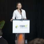 A woman speaks at a podium with a cgaef sign, in front of a black curtain.