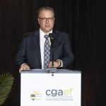 Man in suit speaking at podium with cgaef logo on front, black background behind him.