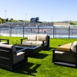 Modern outdoor seating area on grass overlooking a racetrack under a clear sky.