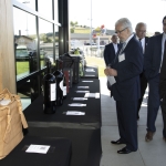 Men in suits view items displayed on tables outside, including wine bottles and gift bags.