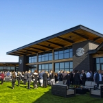 Large group of people socializing on a rooftop patio with modern seating and green turf.