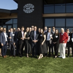 A group of people in formal attire pose together outside a modern building on a sunny day.