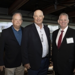 Three men in business attire standing together at an indoor event or conference.