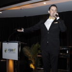 A man in a suit speaks into a microphone on stage at a cgaef event.