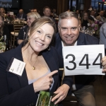 Smiling woman and man holding a sign with the number 344 at an indoor event.