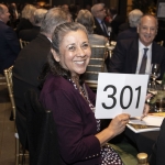 Smiling woman at an event holds up a bidding card with the number 301.