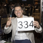 Smiling man holding a sign with 334 and giving a thumbs up at an event.